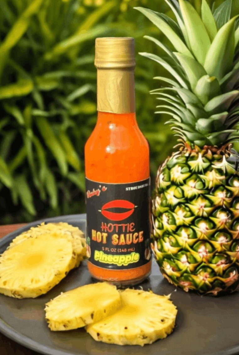 A bottle of hot sauce next to pineapple and another bottle.