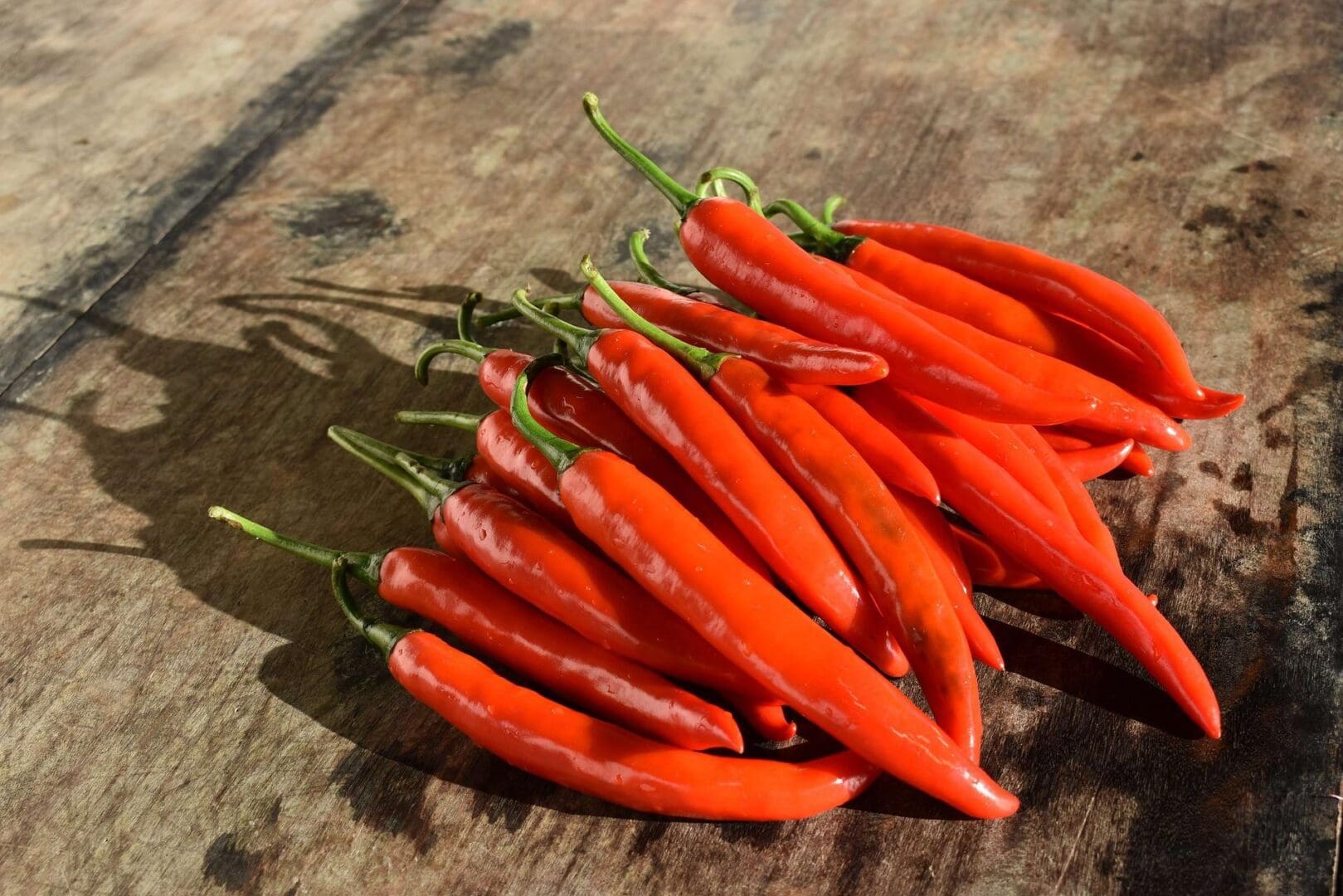 A bunch of fresh red chili peppers is placed on a wooden surface.