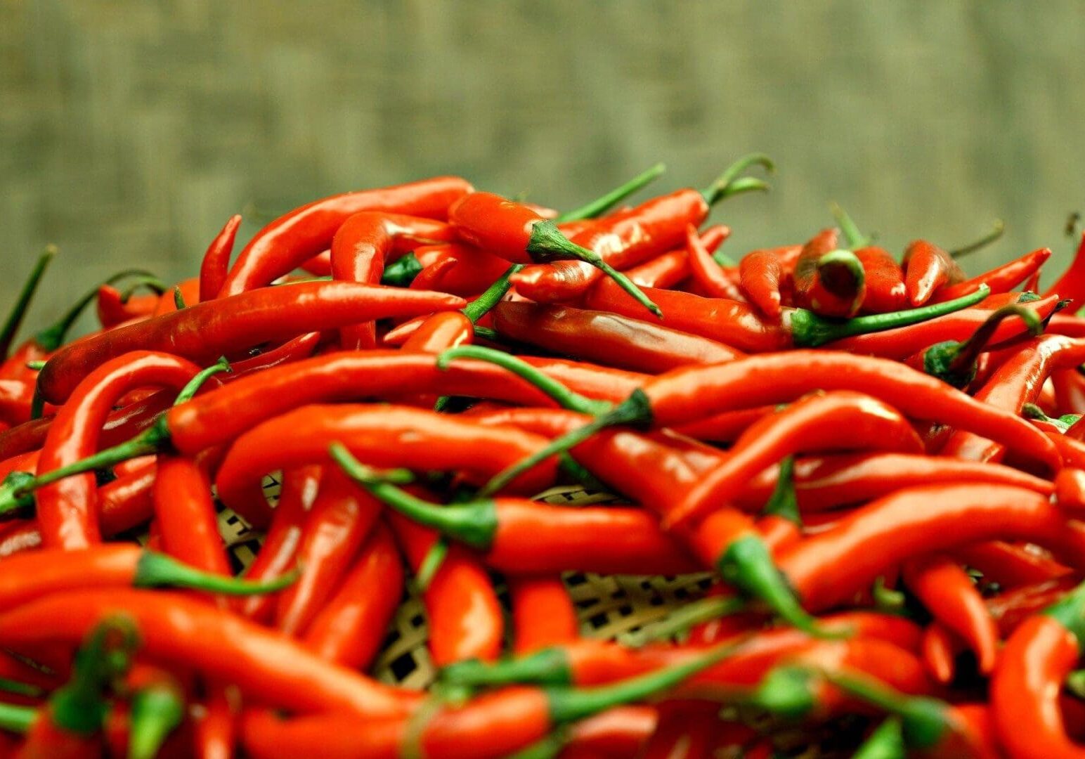 A close-up of a pile of fresh red chili peppers with green stems against a blurred background.