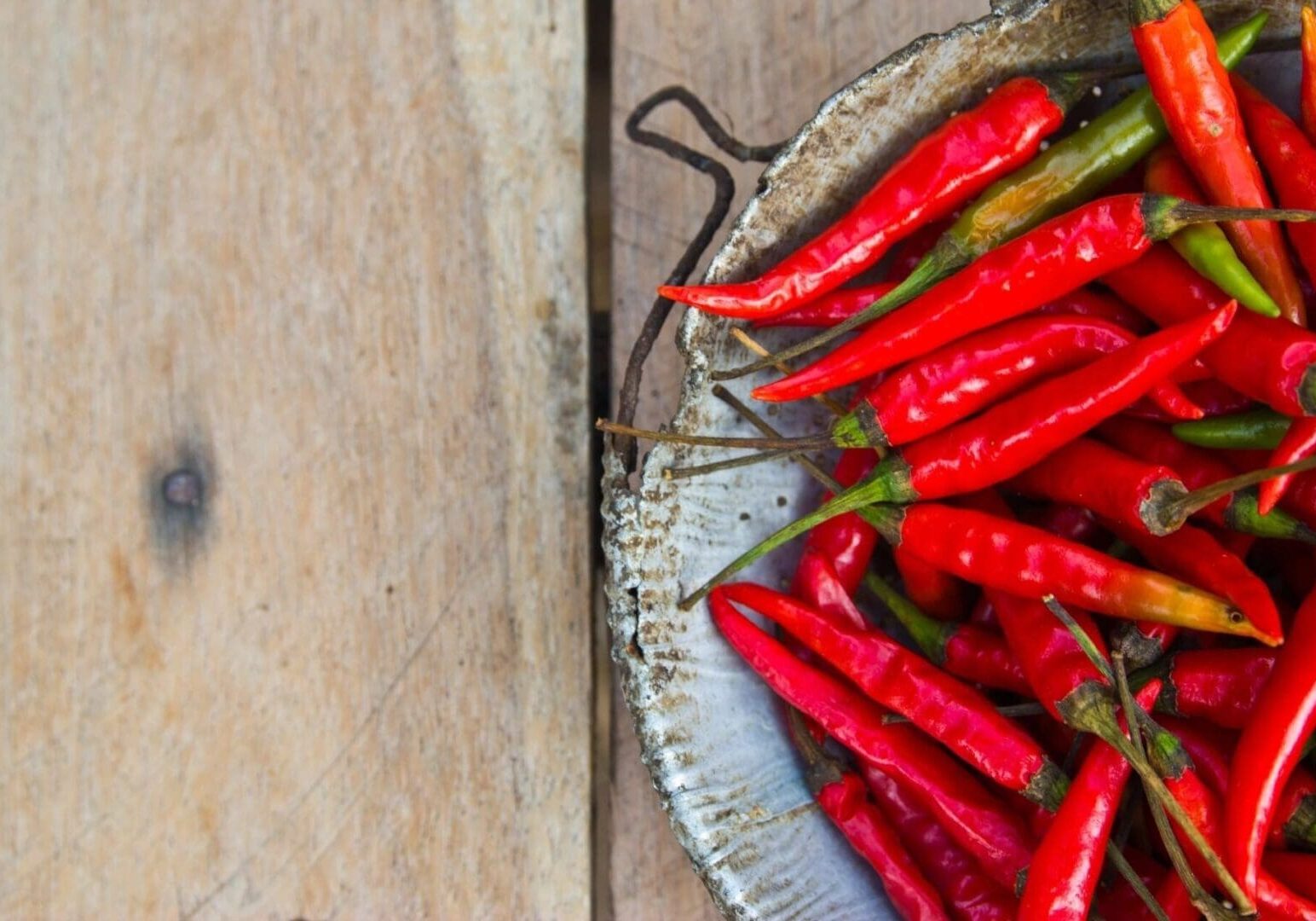 A metal plate sits on a wooden surface, filled with vibrant red and a few green chili peppers.